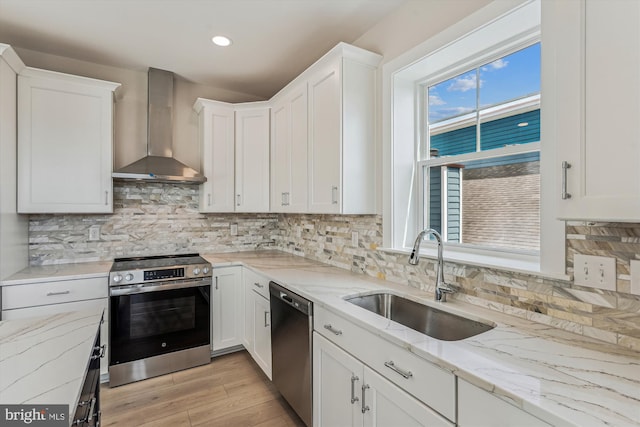 57 Bayside Dr, Fenwick Island, DE 19944 - kitchen featuring stainless steel appliances, wall chimney range hood, a sink, light wood-type flooring, and white cabinetry