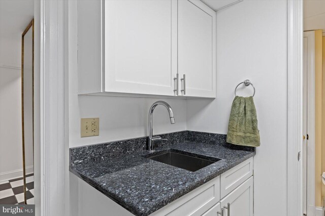 kitchen with a sink, white cabinets, dark stone countertops, and tile patterned floors