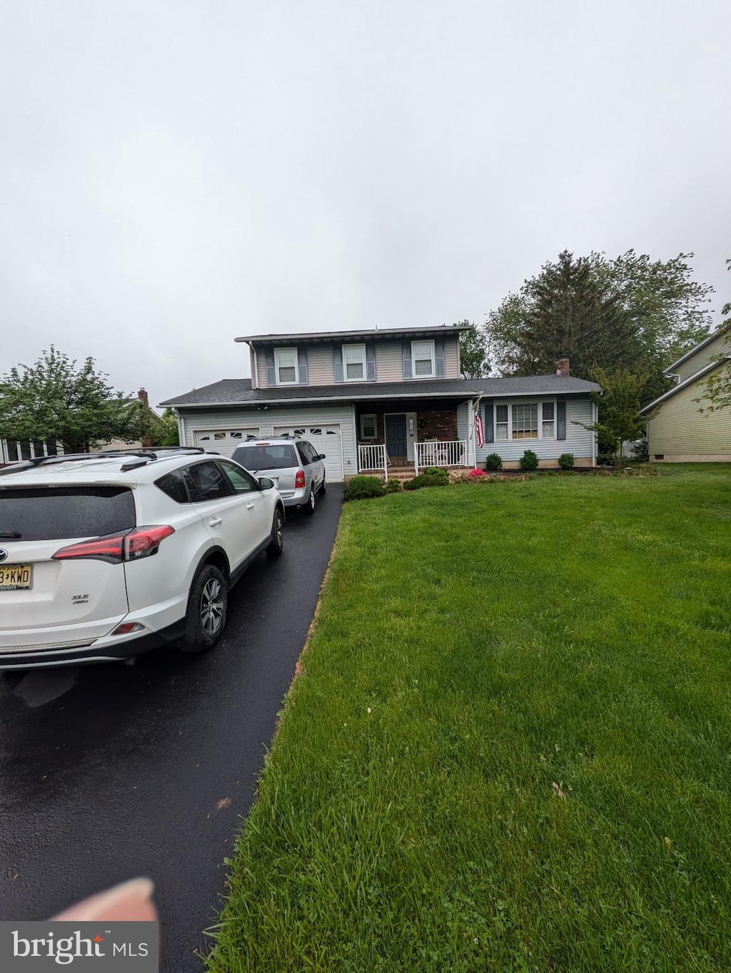 traditional-style house with a garage, a porch, a front lawn, and driveway