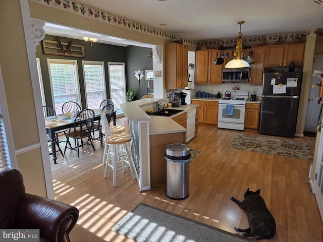kitchen with white appliances, a sink, light countertops, light wood-style floors, and a peninsula