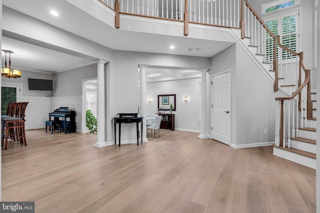 entryway featuring decorative columns, stairway, light wood-style floors, a chandelier, and a towering ceiling