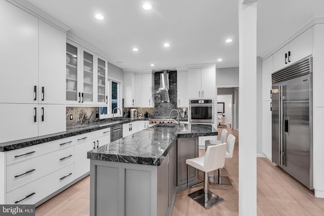 kitchen featuring stainless steel appliances, wall chimney exhaust hood, recessed lighting, backsplash, and light wood-style flooring