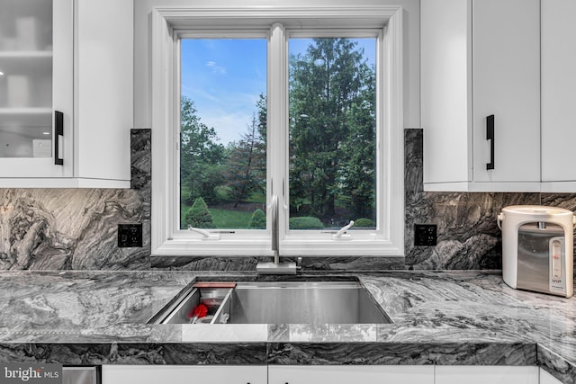 kitchen featuring a sink, white cabinetry, backsplash, and dark stone counters
