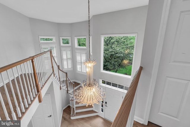 stairway with plenty of natural light, wood finished floors, a chandelier, and baseboards