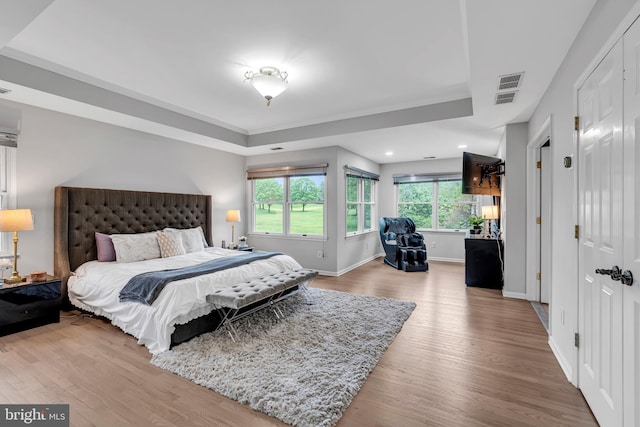 bedroom with a tray ceiling, wood finished floors, baseboards, and crown molding