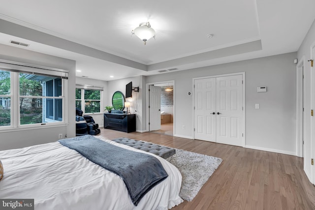 bedroom with a tray ceiling, wood finished floors, baseboards, connected bathroom, and ornamental molding