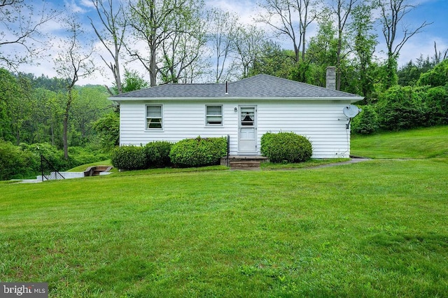 rear view of house featuring a yard, a chimney, and a shingled roof