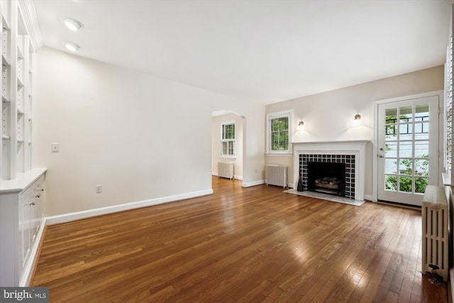 unfurnished living room with radiator, hardwood / wood-style floors, plenty of natural light, and arched walkways