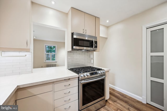 kitchen featuring stainless steel appliances, radiator, light countertops, wood finished floors, and backsplash