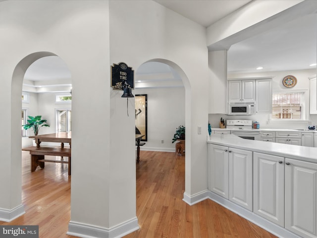 37 Sussex St, Rehoboth Beach, DE 19971 - kitchen with white appliances, arched walkways, white cabinetry, light countertops, and light wood finished floors