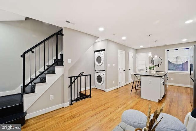 living area with stacked washer / drying machine, baseboards, light wood-type flooring, recessed lighting, and stairs