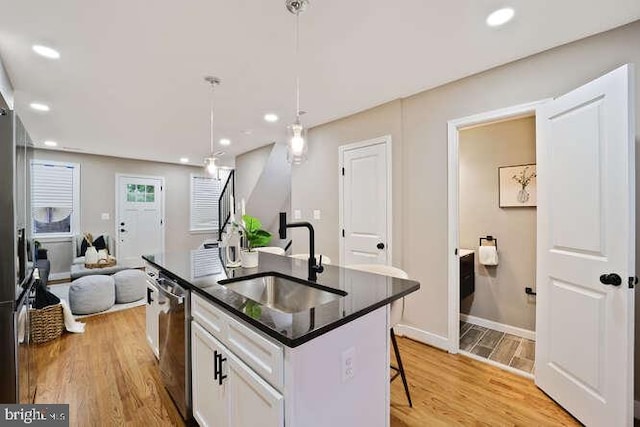 kitchen featuring a sink, light wood-type flooring, stainless steel dishwasher, white cabinetry, and a kitchen bar