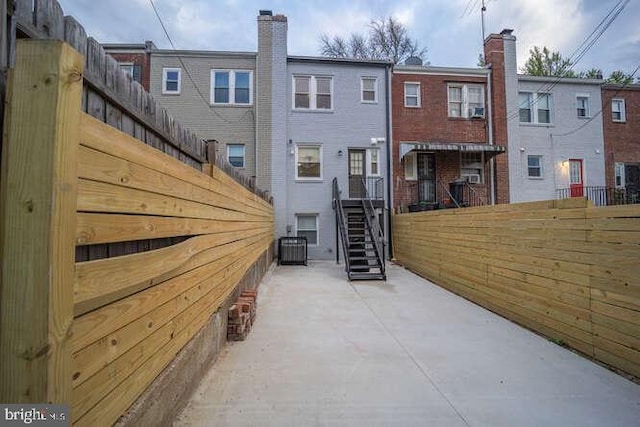 rear view of house featuring fence, central AC unit, brick siding, and stairway