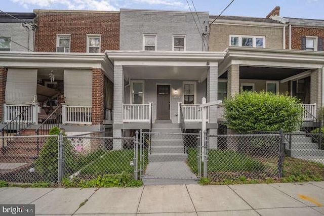 townhome / multi-family property featuring a porch, brick siding, a gate, and a fenced front yard
