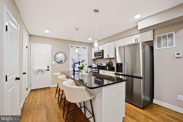 kitchen featuring appliances with stainless steel finishes, a breakfast bar, white cabinetry, light wood-style flooring, and recessed lighting