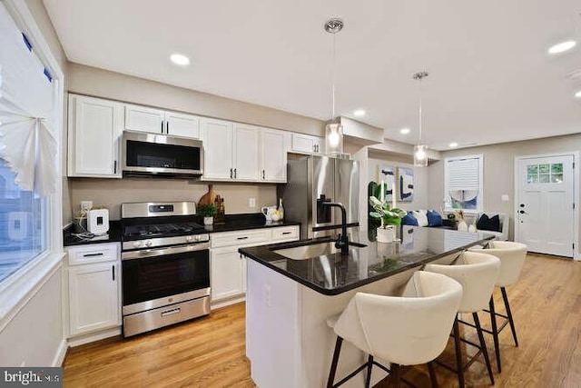 kitchen with stainless steel appliances, a sink, dark countertops, a kitchen bar, and white cabinetry