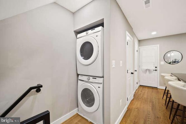 clothes washing area featuring stacked washing machine and dryer, wood finished floors, baseboards, and recessed lighting