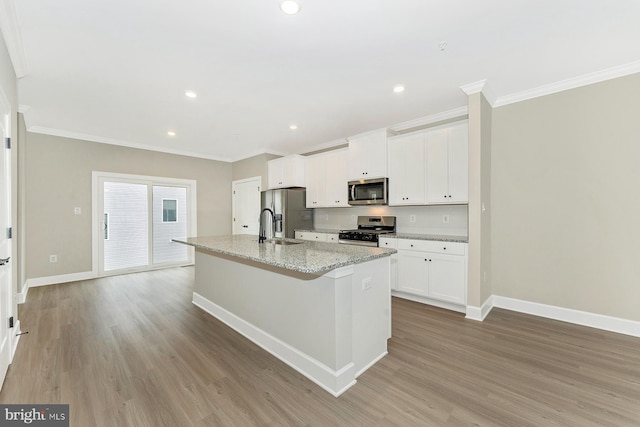 kitchen with stainless steel appliances, a sink, an island with sink, crown molding, and baseboards