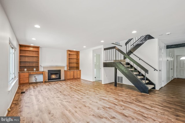 unfurnished living room with light wood finished floors, recessed lighting, stairs, a warm lit fireplace, and baseboards