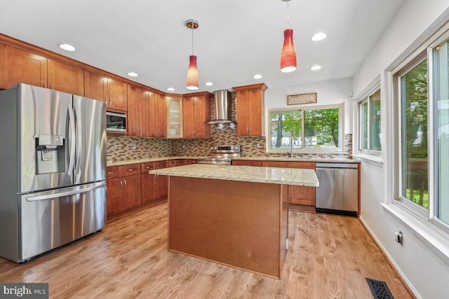kitchen with stainless steel appliances, wall chimney range hood, brown cabinets, a sink, and backsplash