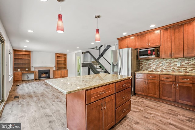 kitchen with stainless steel appliances, tasteful backsplash, light wood-style flooring, hanging light fixtures, and a warm lit fireplace