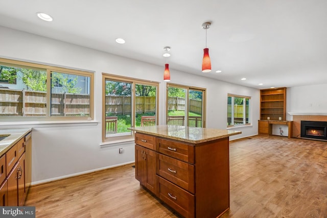 kitchen featuring plenty of natural light, hanging light fixtures, brown cabinets, a lit fireplace, and recessed lighting