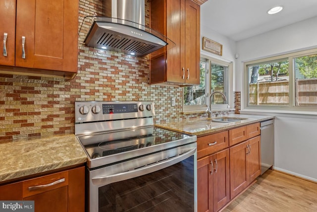 kitchen with appliances with stainless steel finishes, wall chimney exhaust hood, a sink, light stone countertops, and plenty of natural light