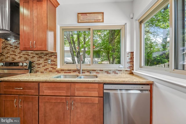 kitchen with appliances with stainless steel finishes, wall chimney exhaust hood, a sink, backsplash, and brown cabinets