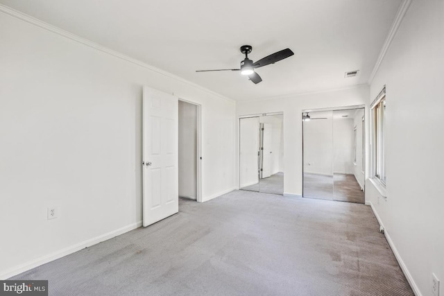 unfurnished bedroom with ornamental molding, multiple closets, carpet, baseboards, and ceiling fan