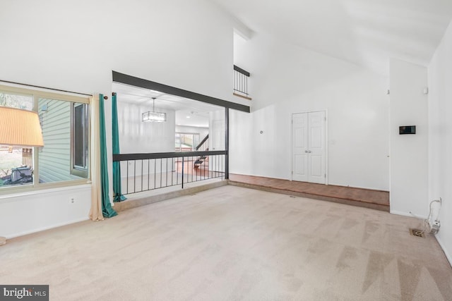 unfurnished living room with carpet floors, high vaulted ceiling, healthy amount of natural light, and baseboards
