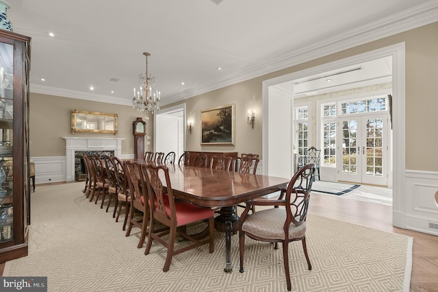 dining area with french doors, wainscoting, ornamental molding, a decorative wall, and a chandelier