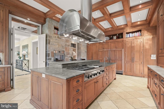 kitchen featuring island range hood, stainless steel gas stovetop, coffered ceiling, brown cabinetry, and beam ceiling