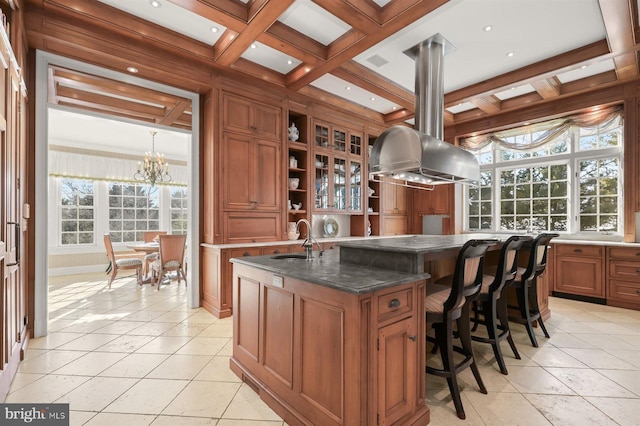 kitchen featuring a sink, brown cabinetry, open shelves, a center island with sink, and beamed ceiling
