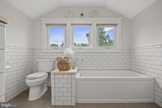 bathroom featuring tile walls, lofted ceiling, toilet, plenty of natural light, and a bath