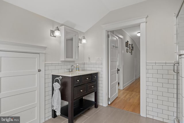 full bathroom featuring lofted ceiling, tile walls, vanity, an enclosed shower, and a wainscoted wall