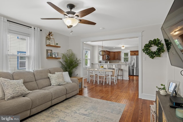 living area featuring ceiling fan, dark wood finished floors, and baseboards