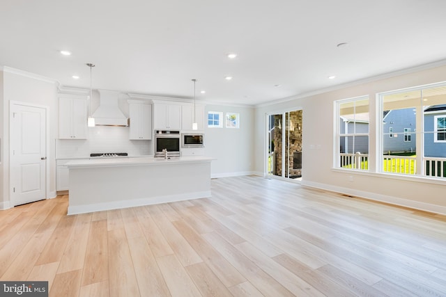 kitchen with custom range hood, appliances with stainless steel finishes, crown molding, a kitchen island with sink, and white cabinets