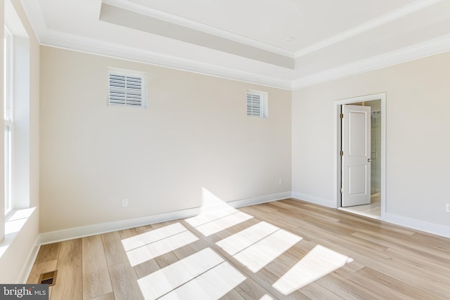 spare room featuring a tray ceiling, ornamental molding, light wood-type flooring, and baseboards
