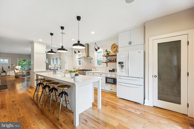 203 Spring Ave, Takoma Park, MD 20912 - kitchen featuring white refrigerator with ice dispenser, wall chimney range hood, light countertops, a breakfast bar, and light wood finished floors