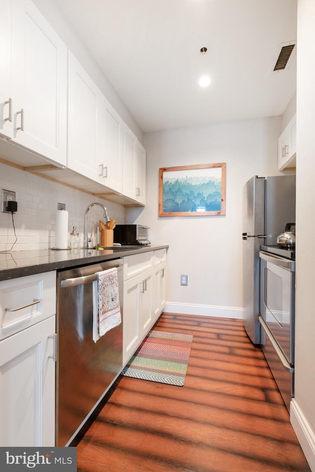 kitchen featuring appliances with stainless steel finishes, baseboards, wood finished floors, backsplash, and white cabinetry