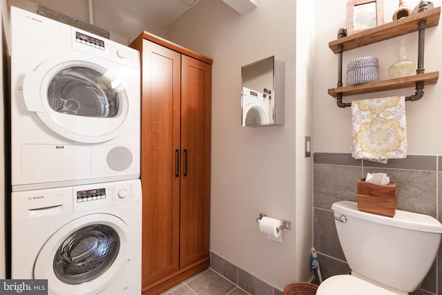 laundry room with stacked washer / drying machine, tile patterned flooring, and tile walls
