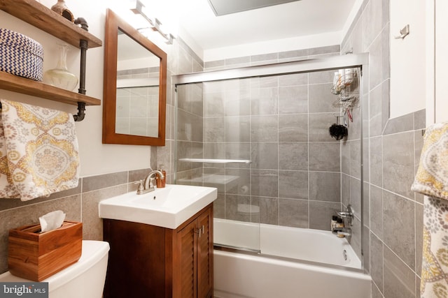 bathroom featuring enclosed tub / shower combo, tile walls, vanity, and toilet