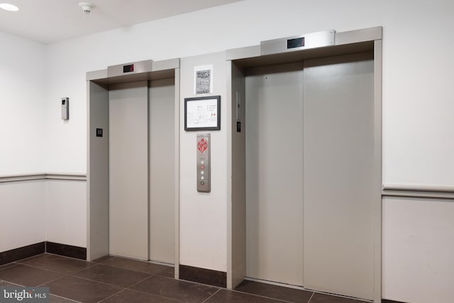 interior space featuring elevator, dark tile patterned floors, and baseboards