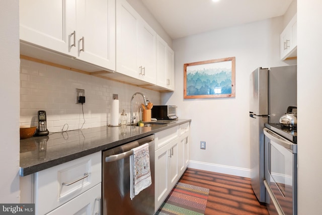 kitchen featuring stainless steel appliances, a sink, backsplash, dark wood-type flooring, and white cabinets