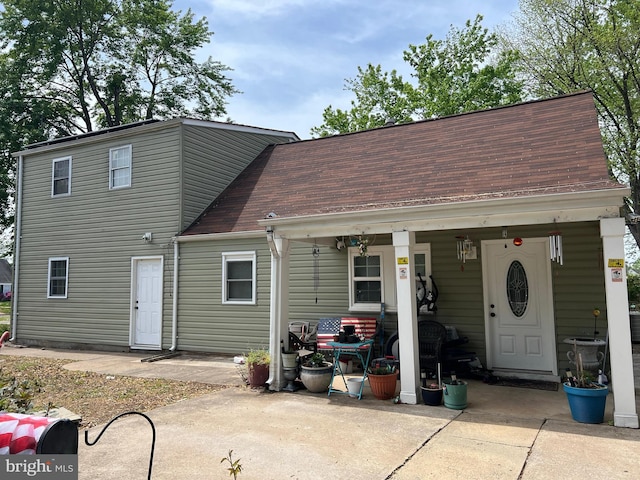 back of property with a shingled roof and a patio