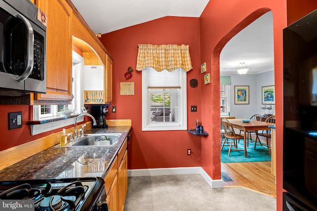 kitchen featuring stainless steel microwave, a sink, black gas stove, arched walkways, and vaulted ceiling