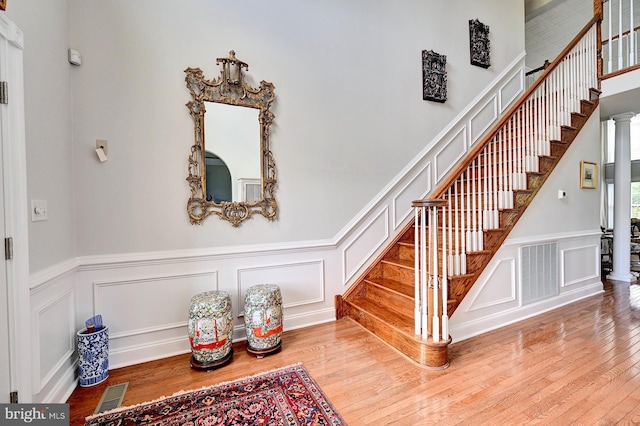 stairs with a decorative wall, hardwood / wood-style floors, wainscoting, and ornate columns