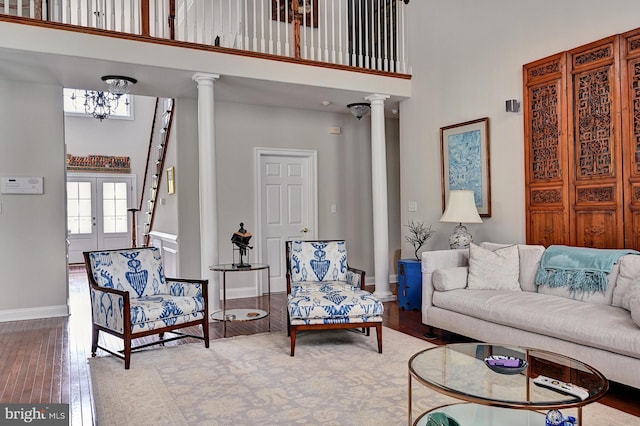 living area with a towering ceiling, decorative columns, a chandelier, and hardwood / wood-style flooring