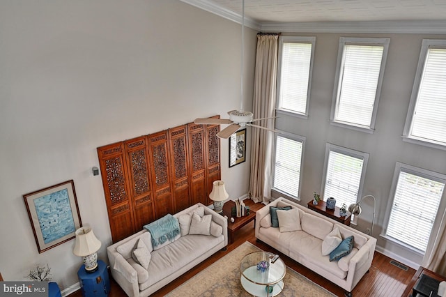 living area with wood finished floors, ornamental molding, plenty of natural light, baseboards, and a towering ceiling