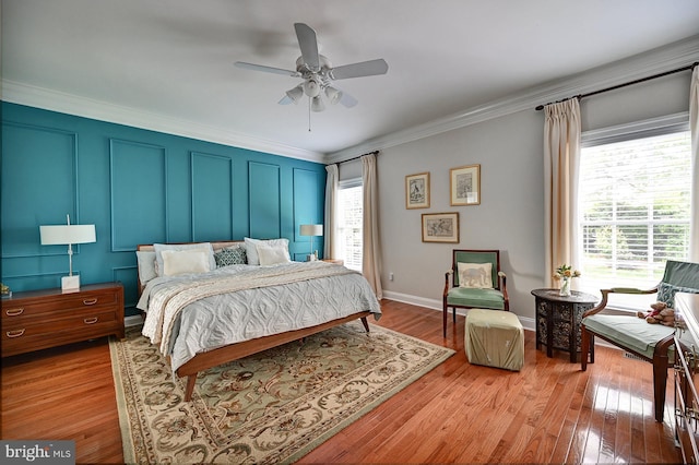 bedroom with crown molding, light wood-style floors, ceiling fan, baseboards, and a decorative wall